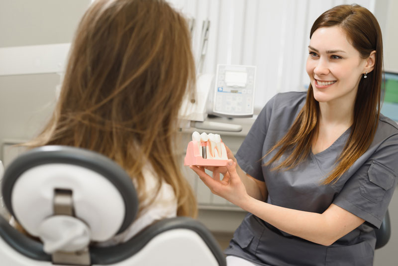 a doctor showing a patient a dental implant model while she tells her the factors that can affect her dental implant treatment.